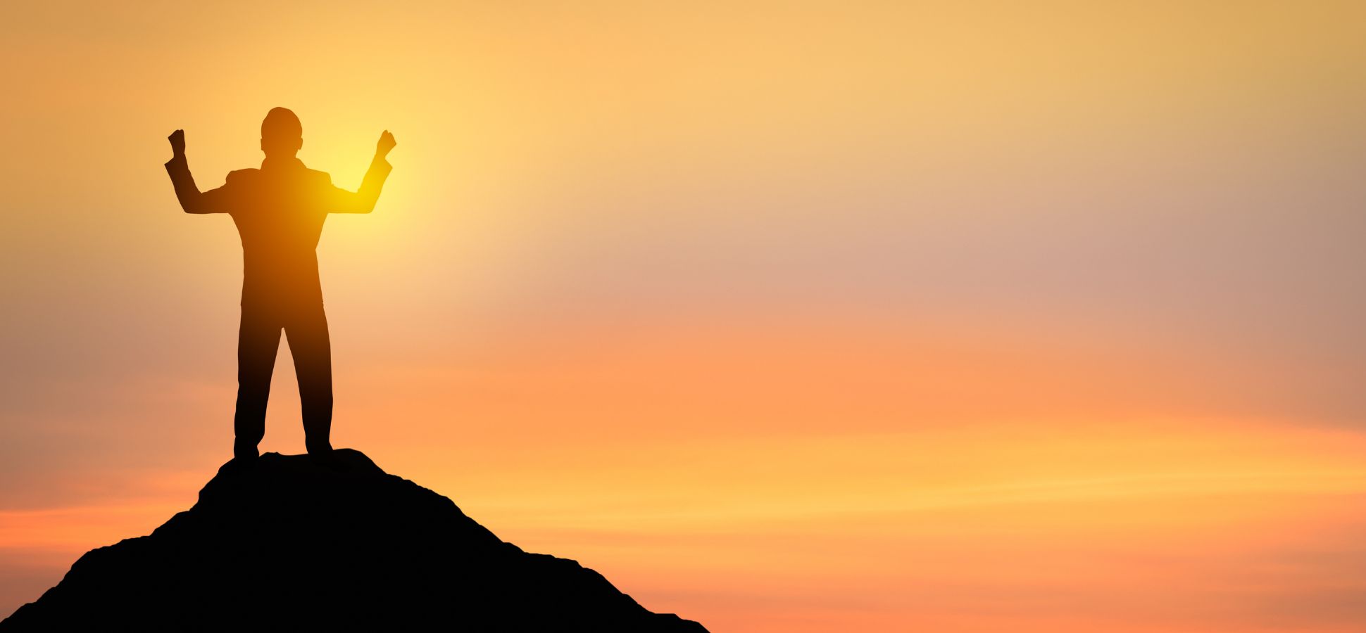 A silhouette of a person standing triumphantly on a mountaintop at sunrise, with arms raised in victory against a vibrant orange and yellow sky.