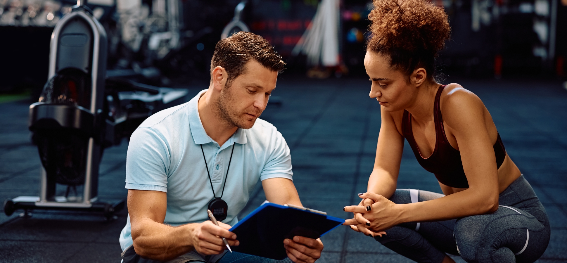 Personal instructor and sportswoman analyzing an exercise plan in a gym.