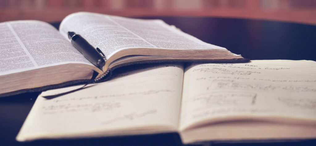 Open book and notebook with pen on desk