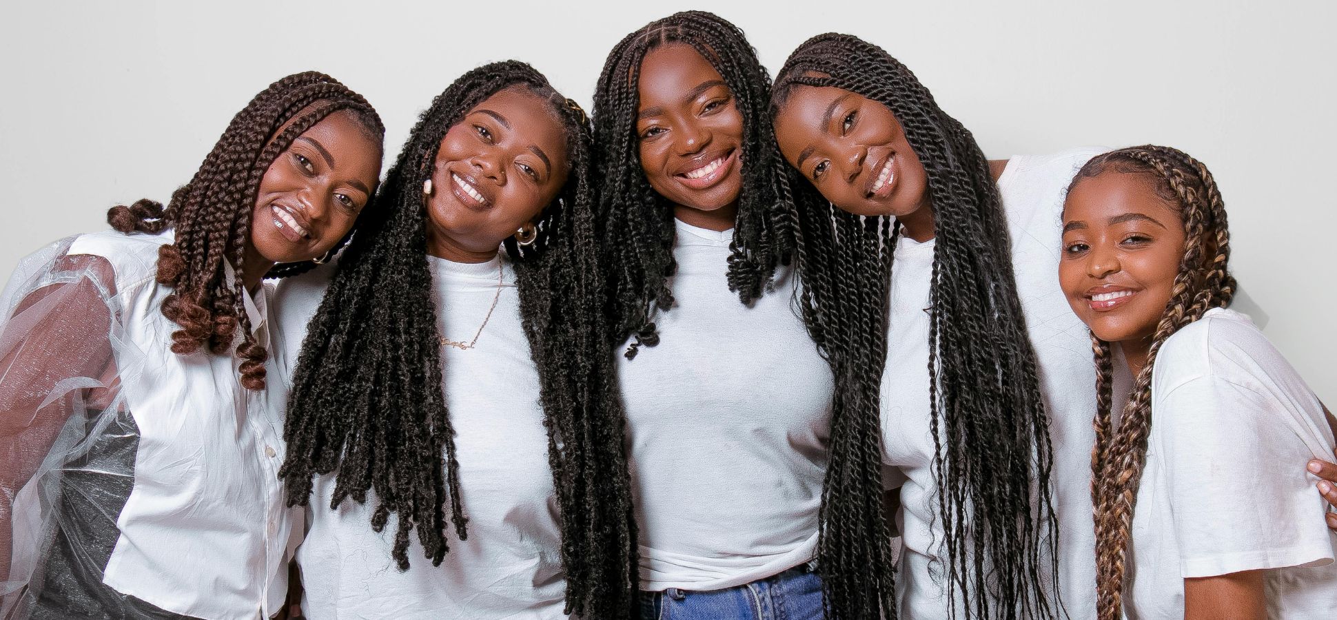 That image features five young women, all appearing to be of African descent, posing together and smiling warmly at the camera. They are all wearing white tops and have long, dark, braided hairstyles.