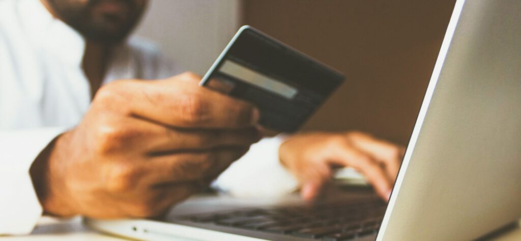 Person holding a credit card while shopping online for tech gifts on a laptop.