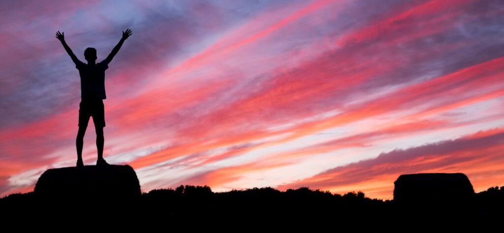 Silhouette man success arms raised sunset sky