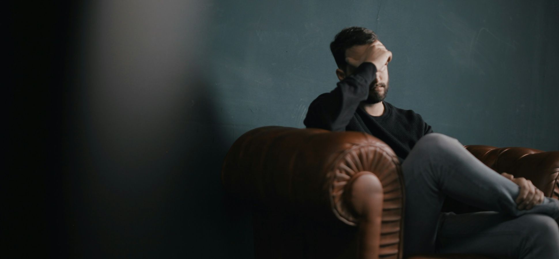 Anxious man sitting on a sofa holding his forehead in distress.
