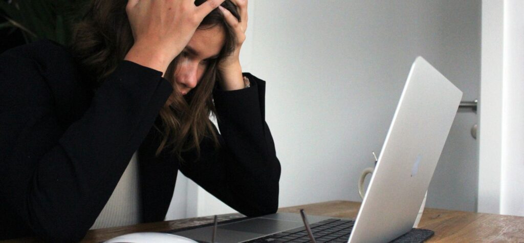 Stressed professional holding their head in frustration while working at a laptop.