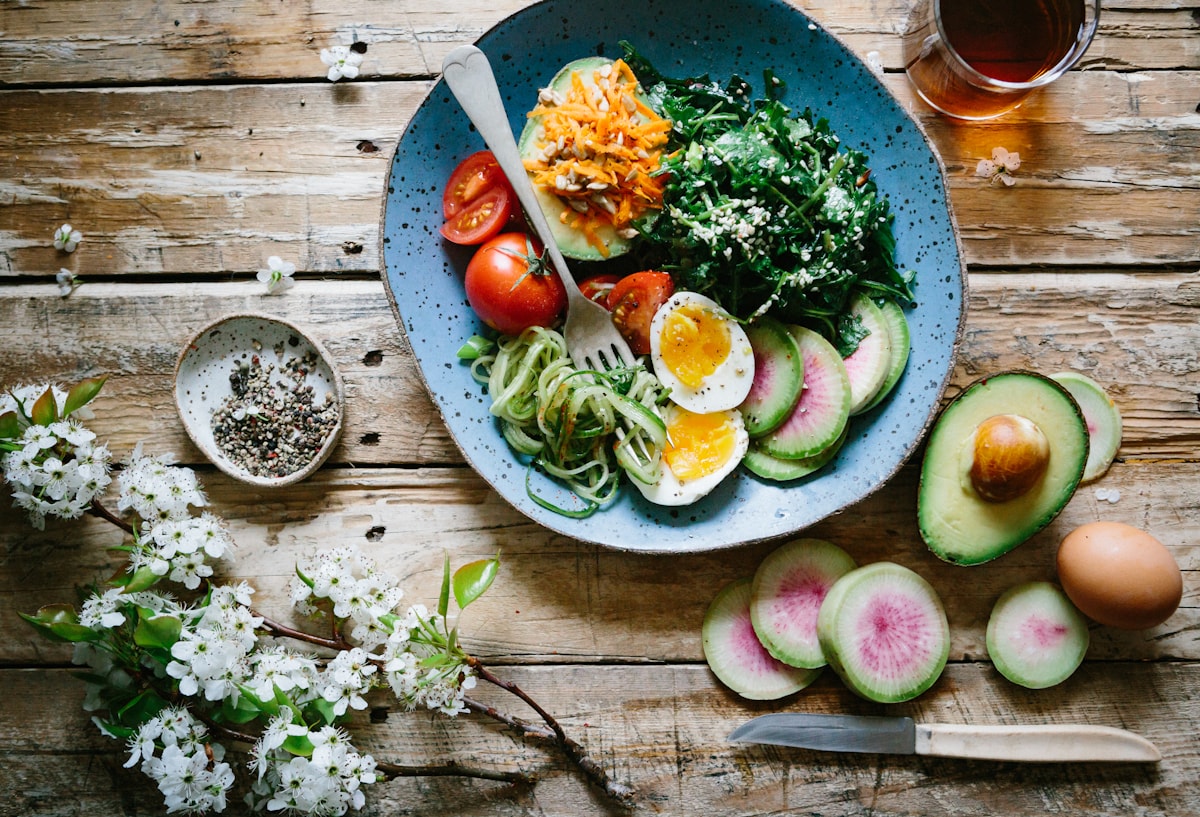 A solo girl dinner bowl with avocado, egg, and vegetables on a rustic wood table