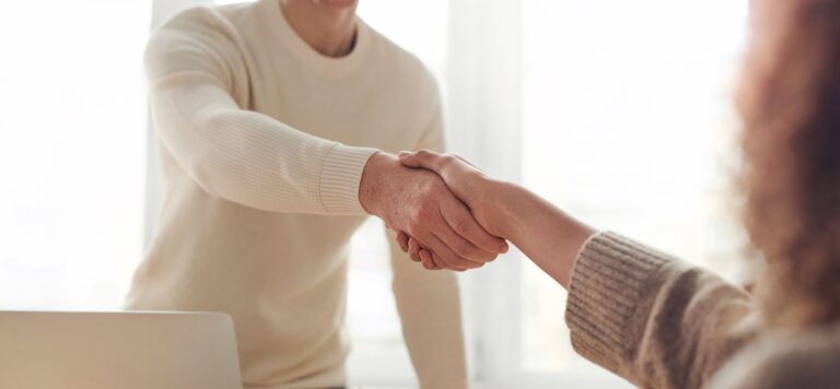 Two founders shaking hands over an acquihire deal at a startup office