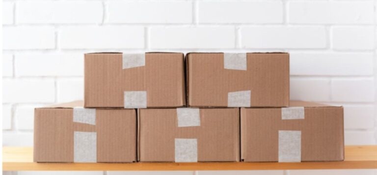 Plain taped cardboard boxes stacked on a wooden shelf against a white brick wall