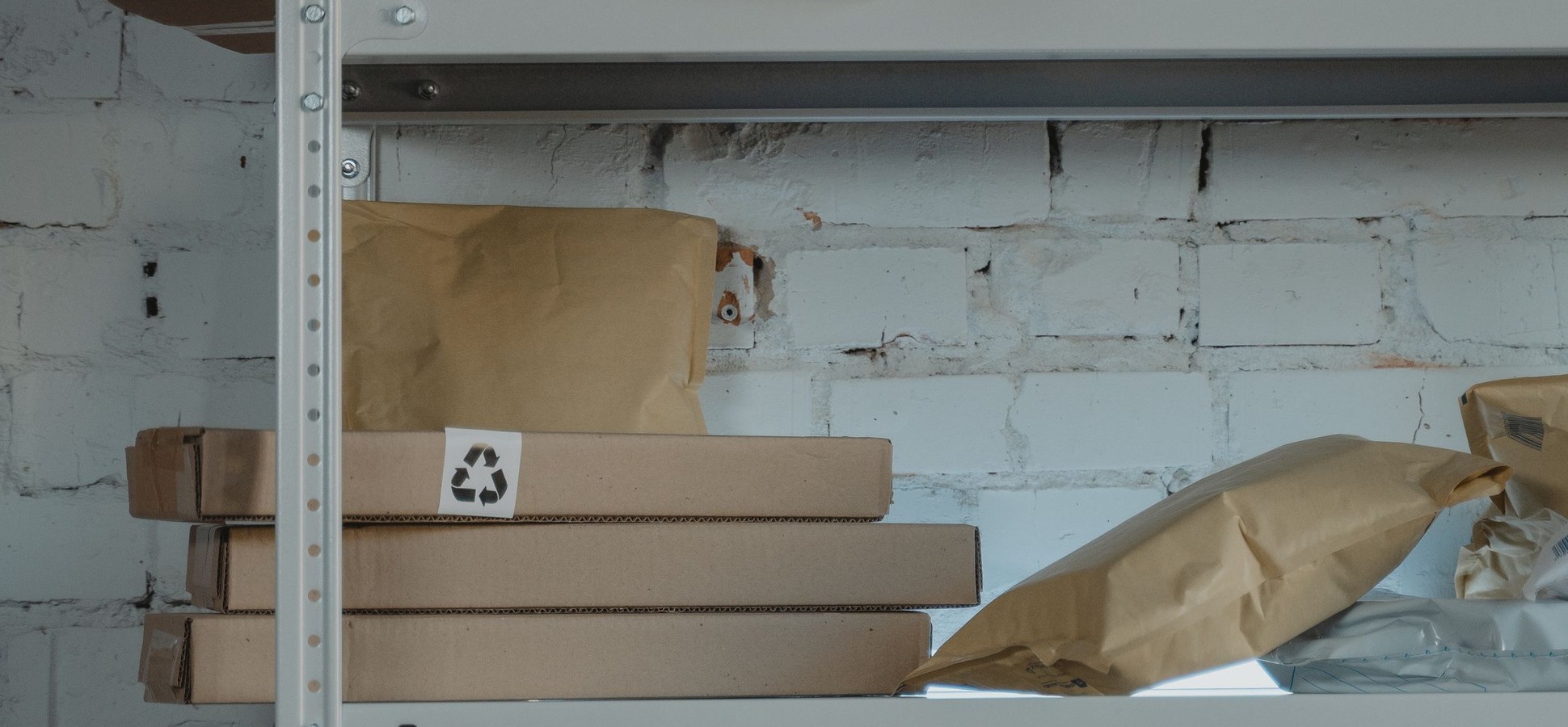 Cardboard boxes and packages stacked on a metal shelf against a white brick wall