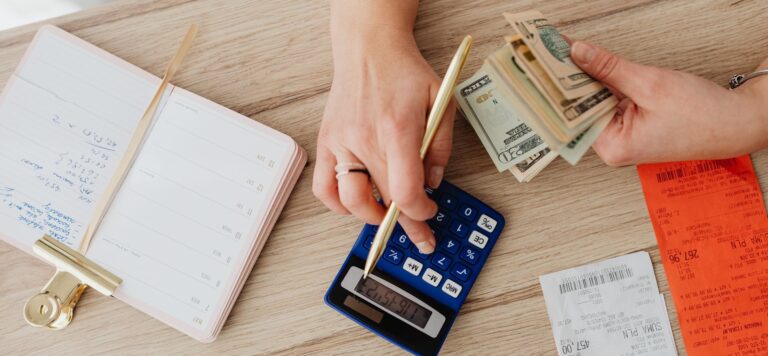 Hands using a calculator beside cash, receipts and a notebook