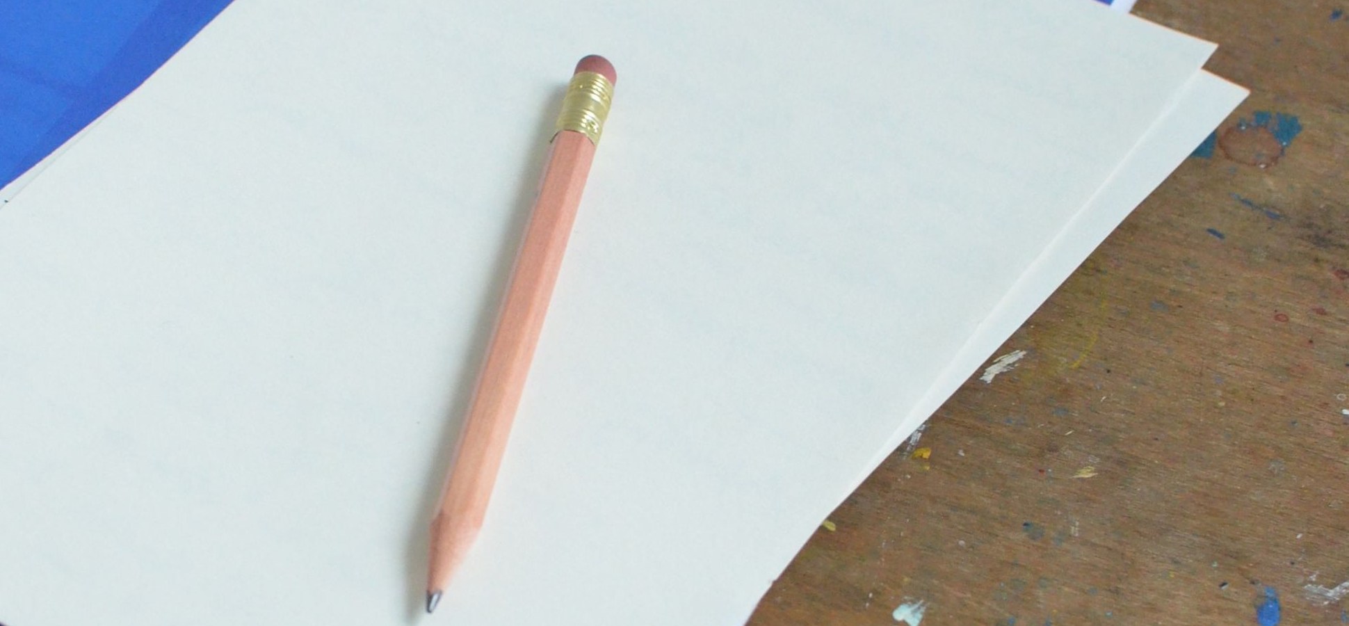 A pencil resting on blank paper sheets on a wooden desk.