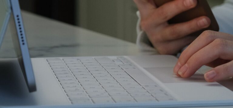 Hands holding a smartphone beside a tablet with a white keyboard case