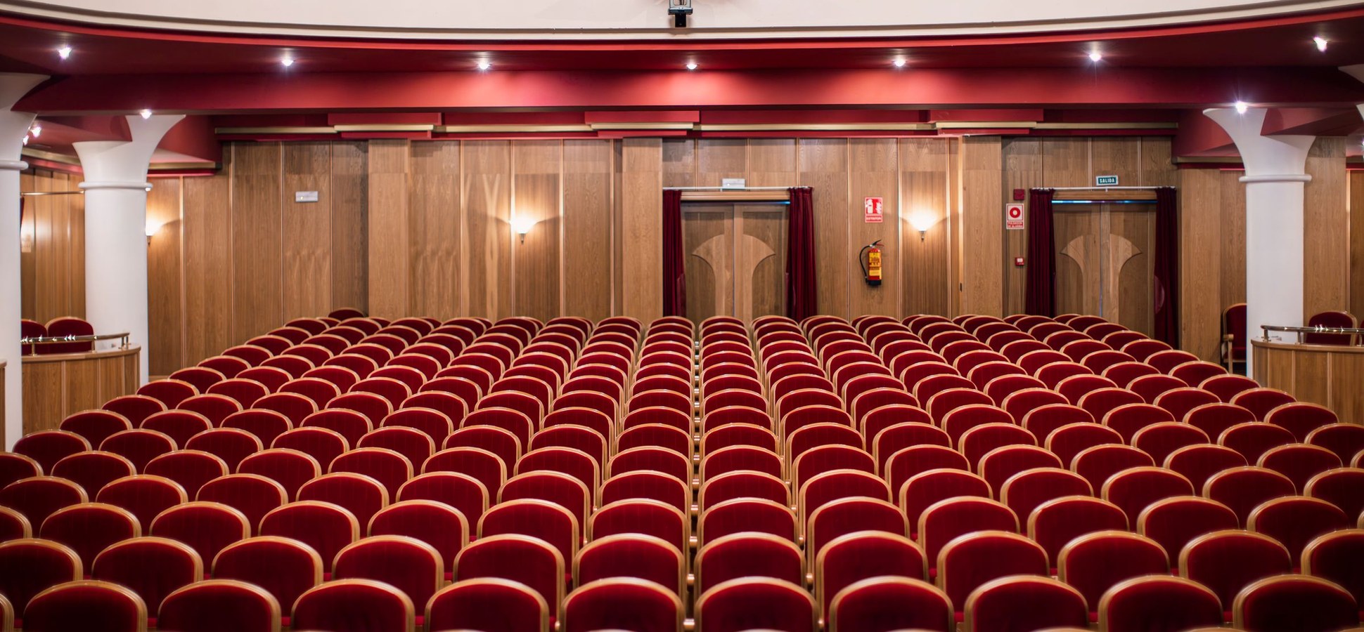 Rows of empty red velvet seats in a theater auditorium with wood-panelled walls