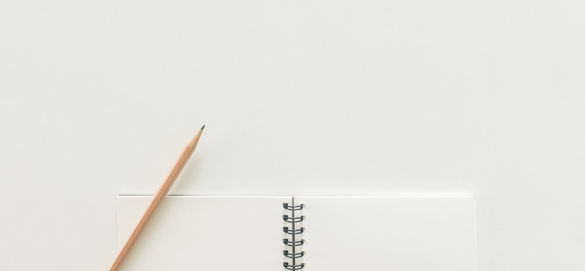 A pencil on a blank spiral notebook against a white background.