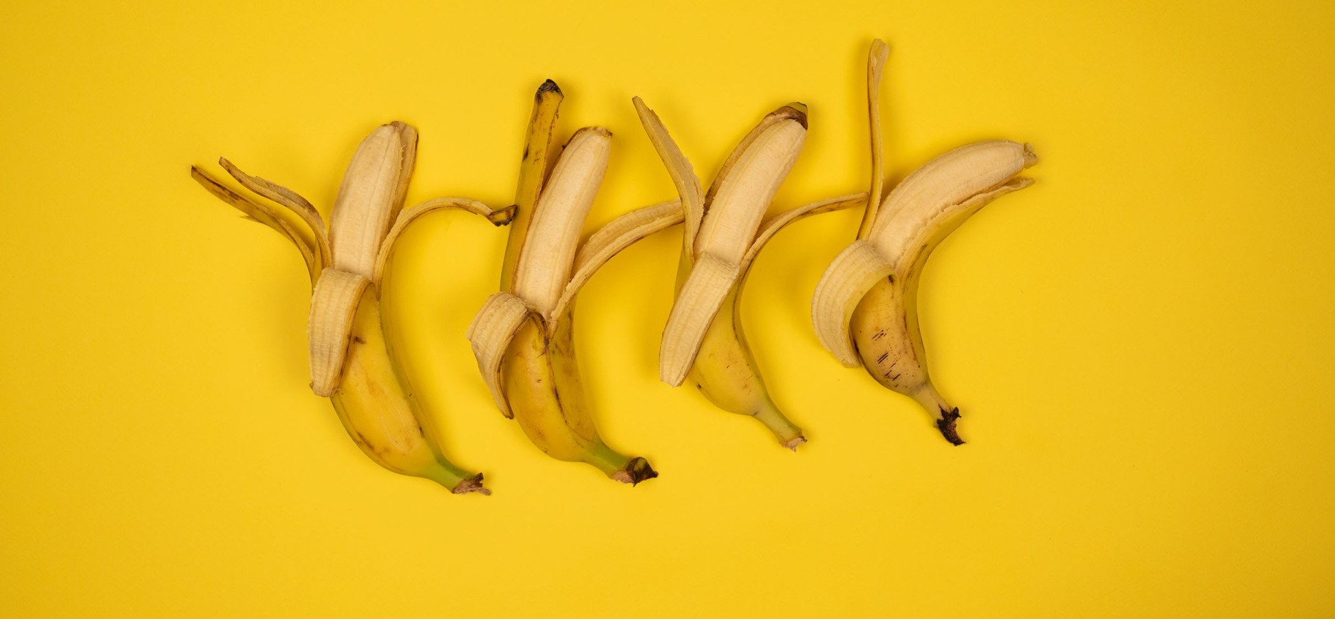 Peeled bananas in a row on a yellow background.